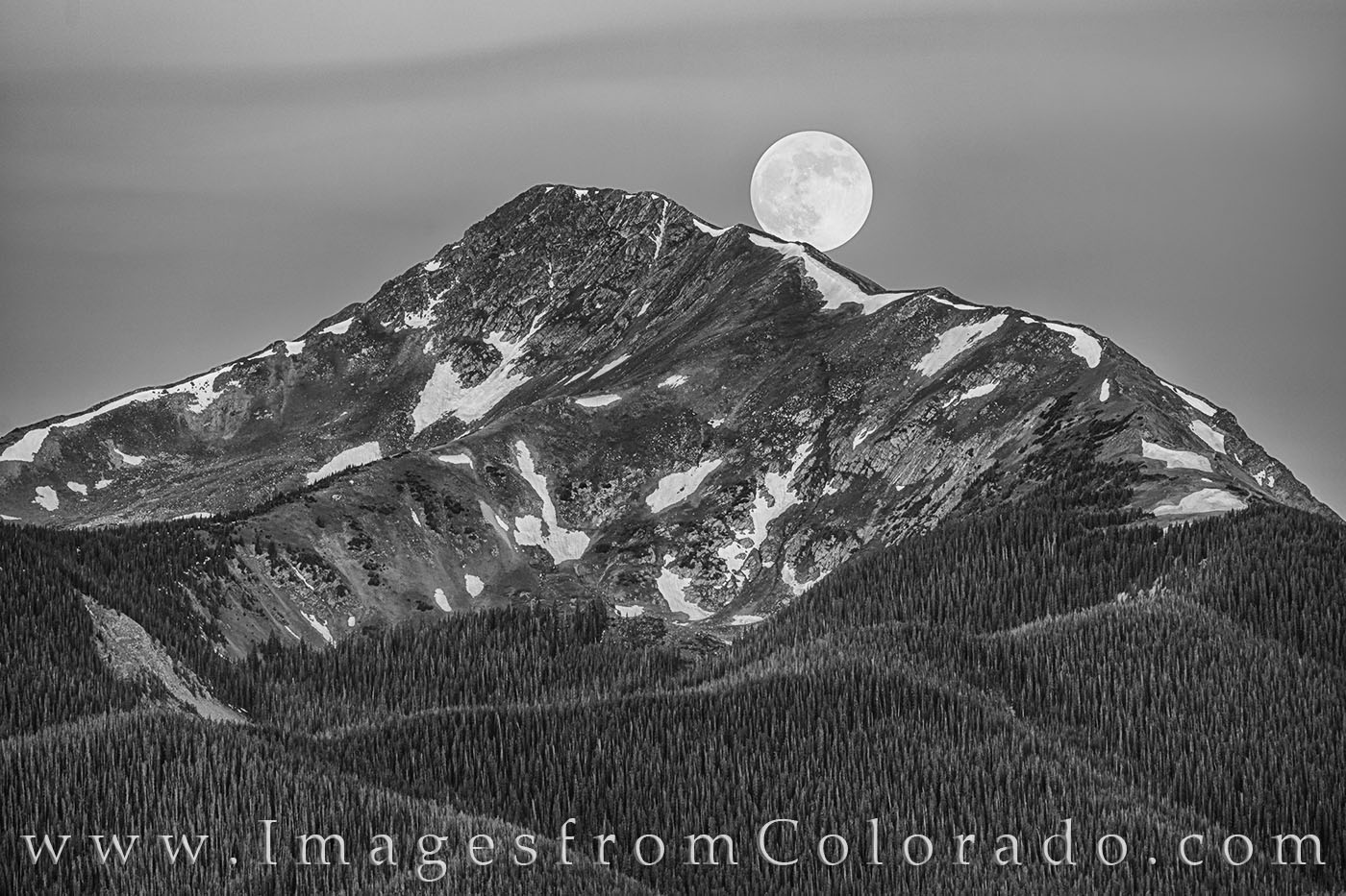 The full moon sets behind Byers Peak in Fraser, Colorado. This black and white photograph shows the iconic landmark of the Fraser...