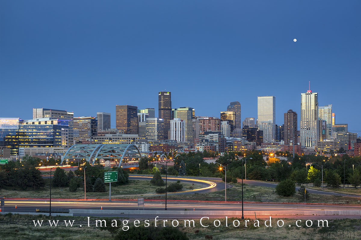 Looking east to the downtown Denver skyline, the nearly full moon rises in the evening. The Speer Boulevard Bridge is in the...