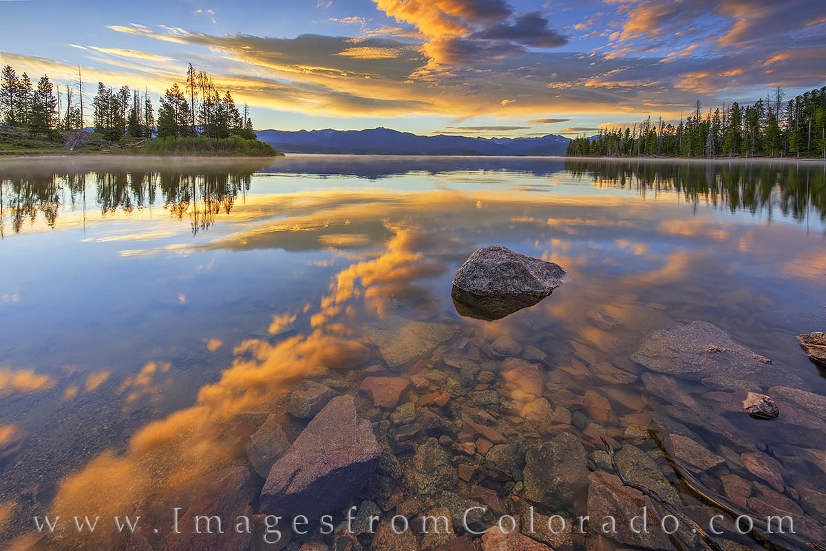 On a glorious morning near Grand Lake, Colorado, the colors of the shined high above as their reflection added color to the still...