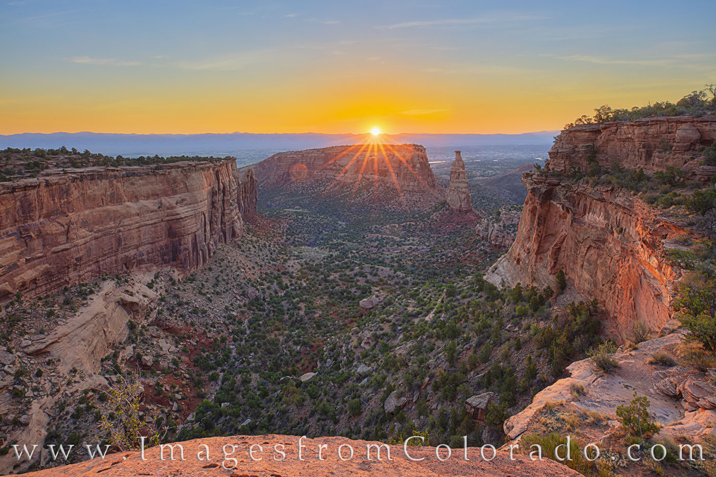 The light of sunrise spreads through the canyon in this morning photograph showing Independence Monument in Colorado National...