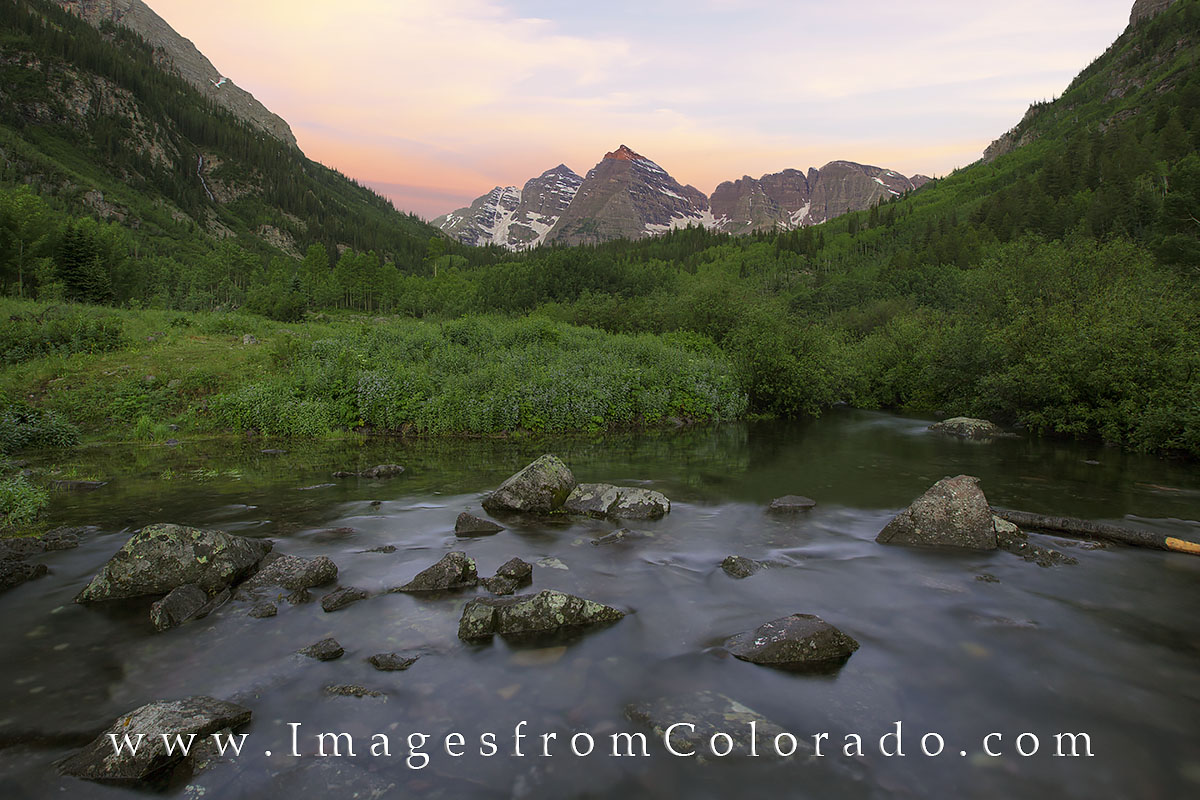 Maroon Creek flows with snowmelt on an early summer morning. In the distance, the Maroon Bells rise into the cool air of the...