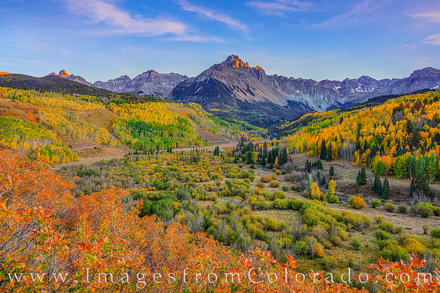 Mount Sneffels rises over 14,000’ into the cool October evening and towers above a valley filled with red and orange scrub...