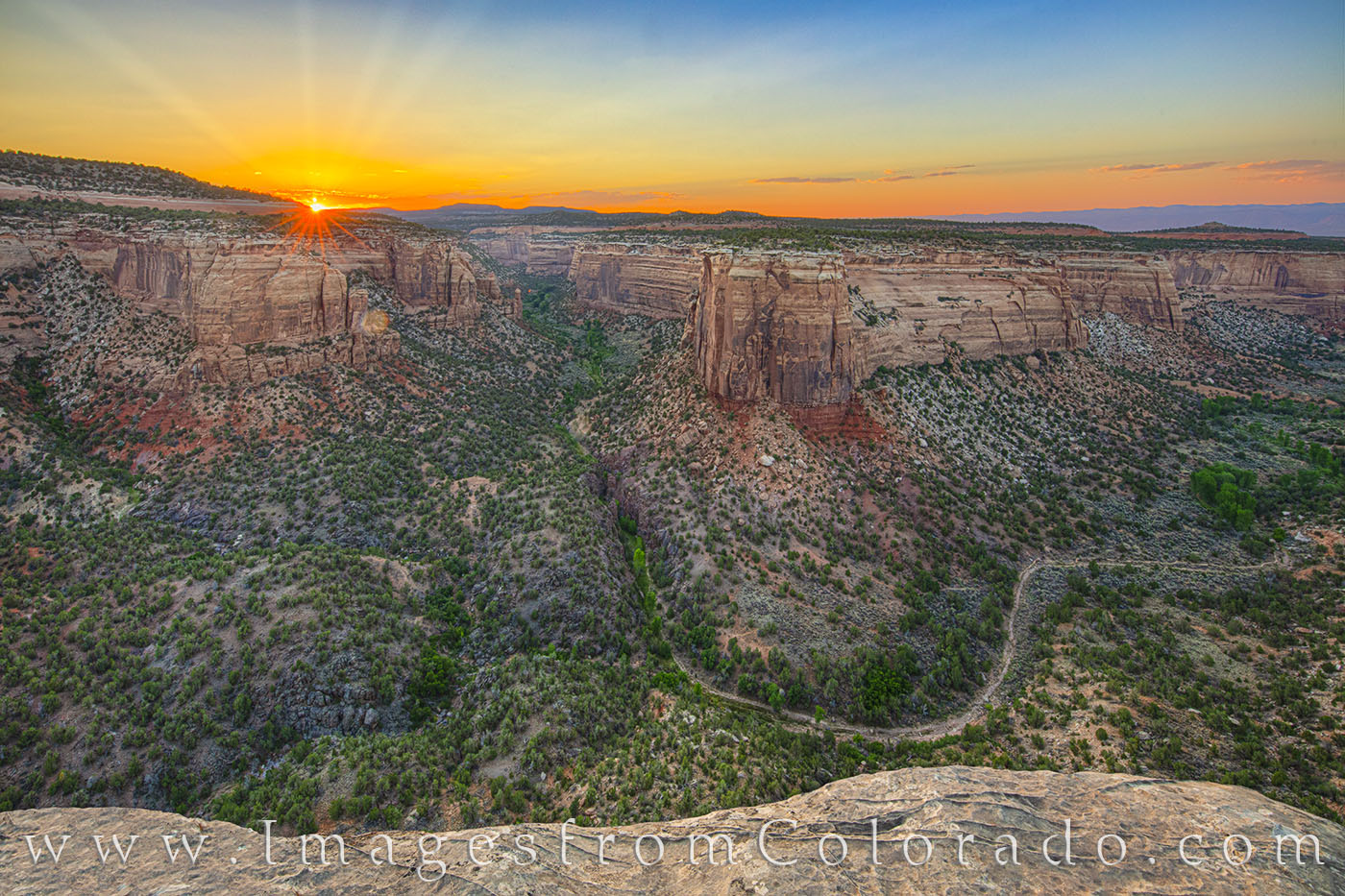 The last rays of sunshite streak up through distant clouds, bringing a glorious end of the day to Colorado National Monument...